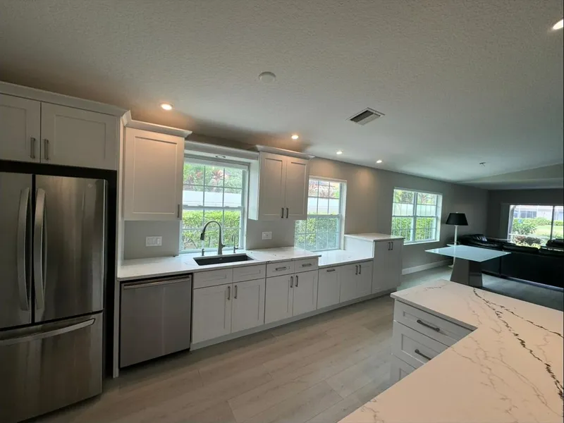 Long white kitchen run with stainless appliances and marble-look island